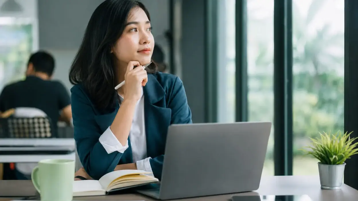 Profesional muda di kantor modern sedang merefleksikan stres kerja awal karier
