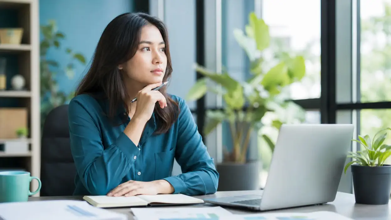 Profesional muda duduk di kantor modern sedang refleksi untuk mengelola stres kerja